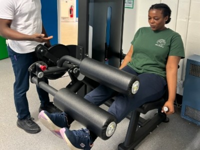 A physiotherapy patient uses a machine to exercise her legs while a physiotherapist watches