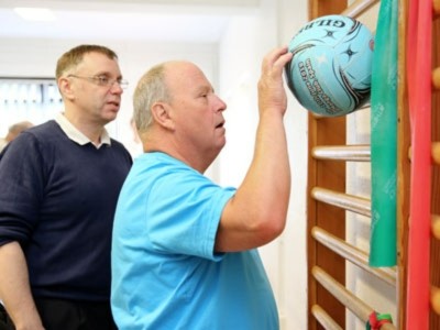 A physiotherapy patient use a ball to exercise his wrist while a physiotherapist watches